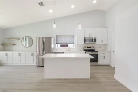 a kitchen with stainless steel appliances granite countertop a stove top oven a sink a refrigerator white cabinets and wooden floor