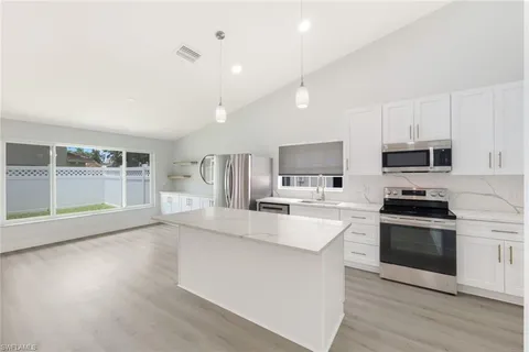 a large kitchen with stainless steel appliances a large counter top a stove a refrigerator cabinets and a wooden floor