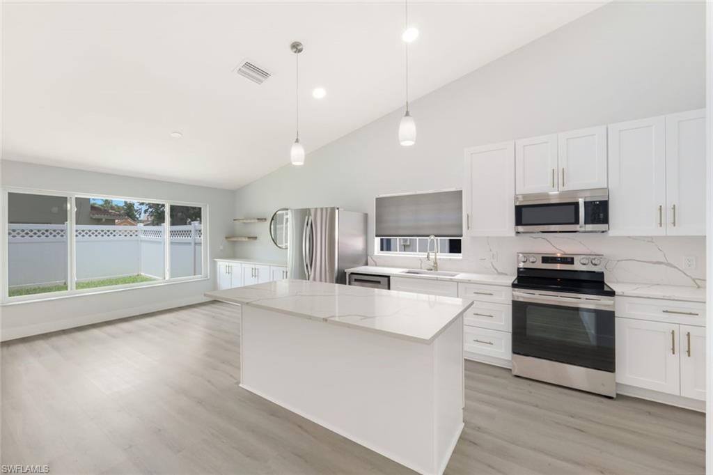 12800 Eagle Pointe Circle Fort Myers, FL 33913 - Photo 9 of 28 a large kitchen with stainless steel appliances a large counter top a stove a refrigerator cabinets and a wooden floor