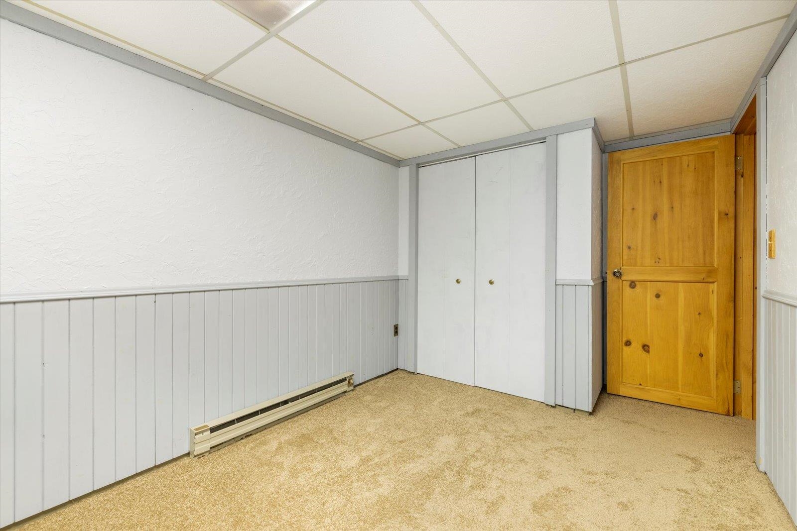236 East Ahola Road Ely, MN 55731 - Photo 14 of 27 Unfurnished bedroom featuring a drop ceiling, baseboard heating, a wainscoted wall, carpet floors, and a closet