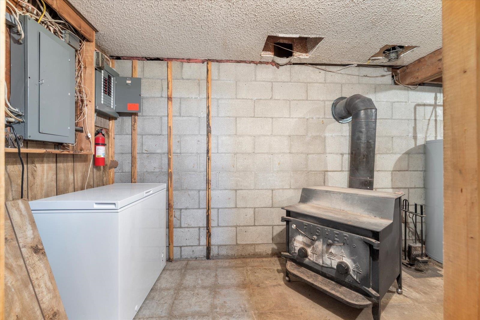 236 East Ahola Road Ely, MN 55731 - Photo 24 of 27 Unfinished below grade area featuring electric panel, a wood stove, water heater, and a textured ceiling