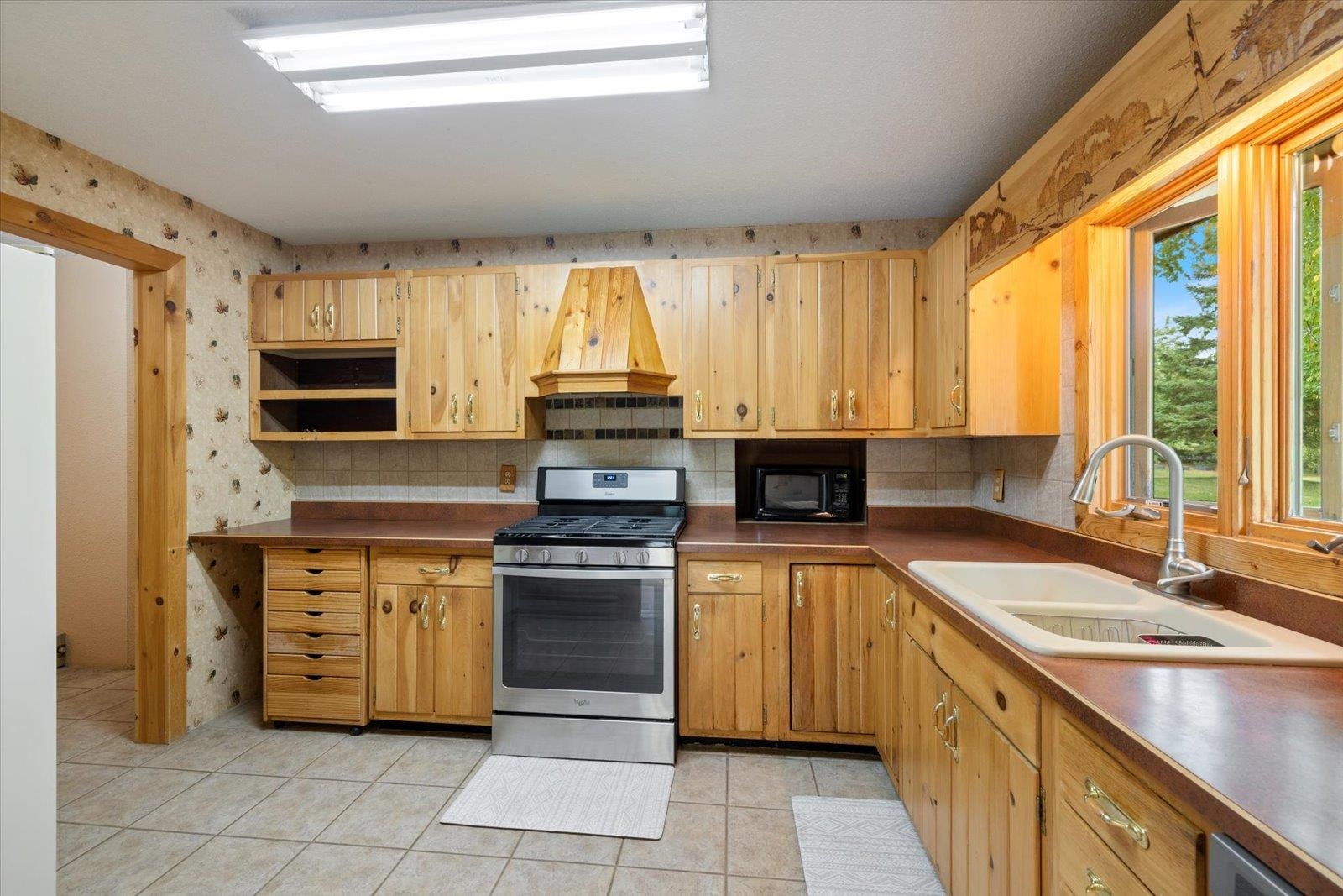 236 East Ahola Road Ely, MN 55731 - Photo 4 of 27 Kitchen with stainless steel range with gas cooktop, light tile patterned floors, tasteful backsplash, wallpapered walls, and custom exhaust hood