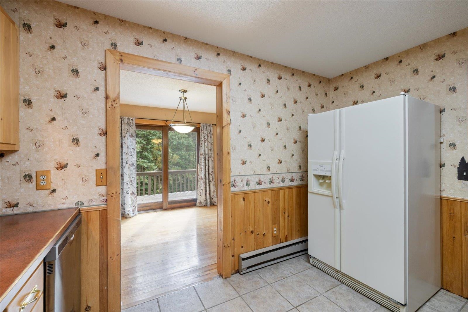 236 East Ahola Road Ely, MN 55731 - Photo 6 of 27 Kitchen featuring white fridge with ice dispenser, wainscoting, baseboard heating, light tile patterned floors, and wood walls