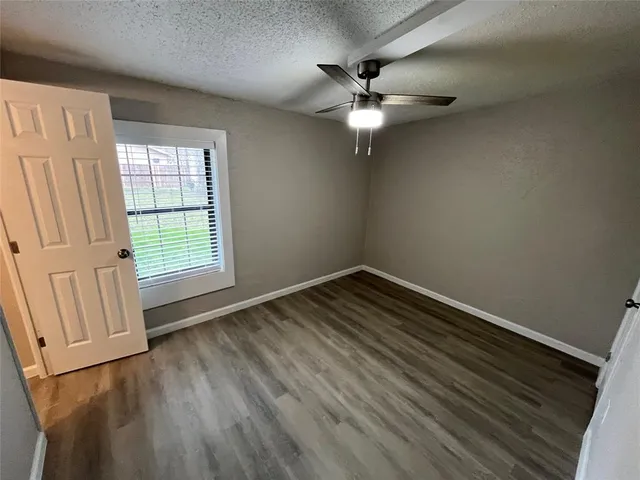 an empty room with wooden floor fan and windows
