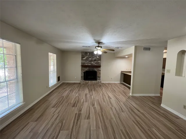 an empty room with wooden floor fireplace and windows