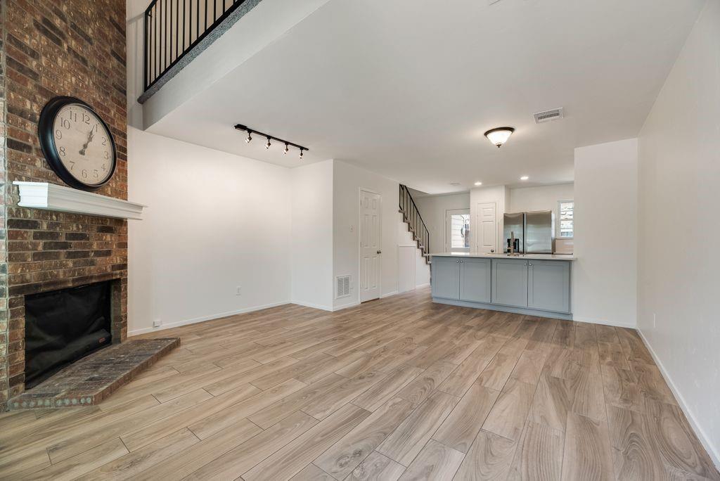 28 Abbey Road Euless, TX 76039 - Photo 5 of 19 Spacious living area featuring a floor-to-ceiling brick fireplace with a white mantel, wood-finish flooring, and a modern kitchen island with light blue cabinetry and a light-toned countertop