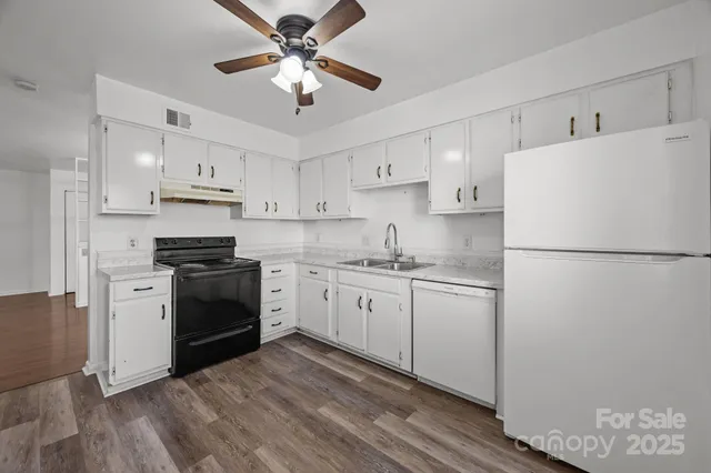 a kitchen with granite countertop a refrigerator a stove a sink and white cabinets