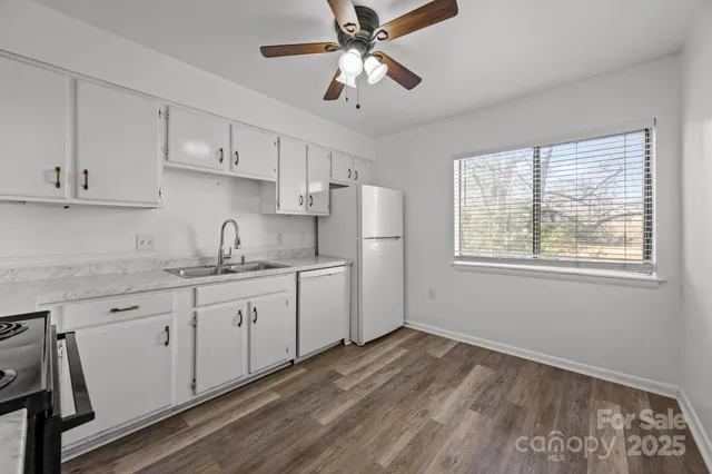 a kitchen with granite countertop white cabinets white appliances a sink and a window