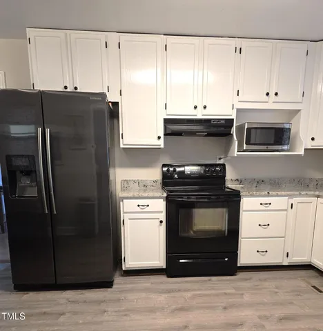 a kitchen with granite countertop a refrigerator stove and white cabinets