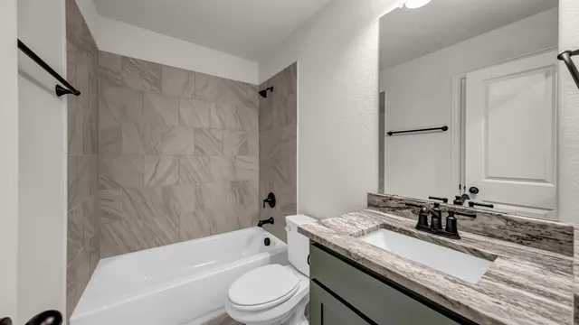 a bathroom with a granite countertop bathtub shower sink vanity mirror and toilet