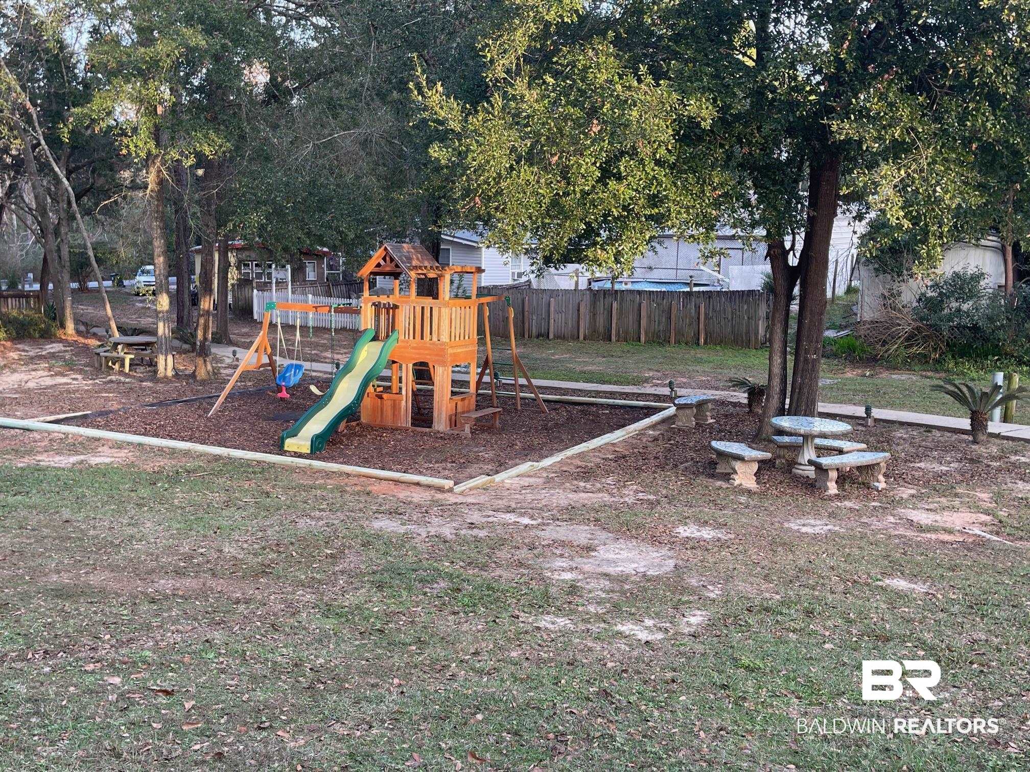 2808 Pine Ridge Drive Lillian, AL 36549 - Photo 35 of 47 Spacious backyard featuring a multi-level wooden playset with slide and swings, a dedicated bark-mulch play area, mature trees, and a concrete picnic table with benches