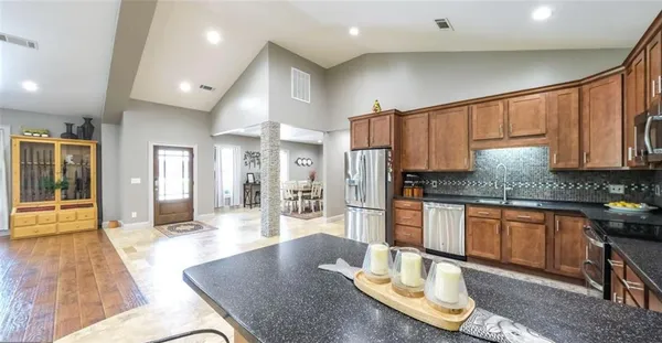 a kitchen with stainless steel appliances granite countertop a stove a refrigerator a sink a dining table and chairs with wooden floor