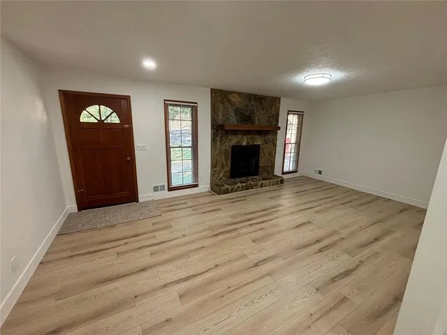 an empty room with wooden floor fireplace and windows