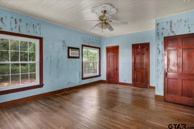a view of an empty room with wooden floor and a ceiling fan