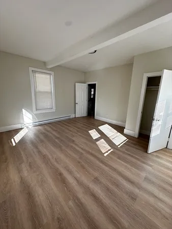 a view of an empty room with window and wooden floor
