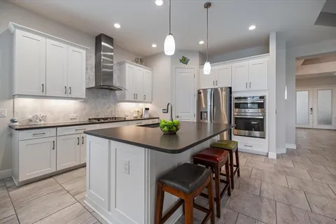 a kitchen with stainless steel appliances granite countertop a sink a stove a refrigerator and island with wooden floor