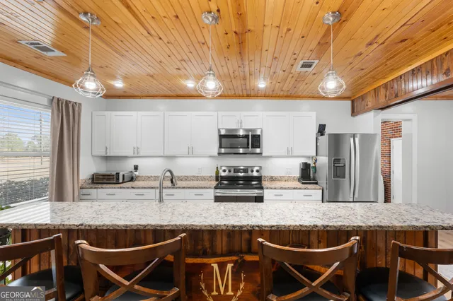 a kitchen with stainless steel appliances granite countertop a sink a stove a refrigerator cabinets and chairs