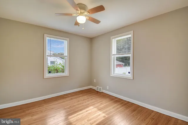 an empty room with wooden floor ceiling fan and windows