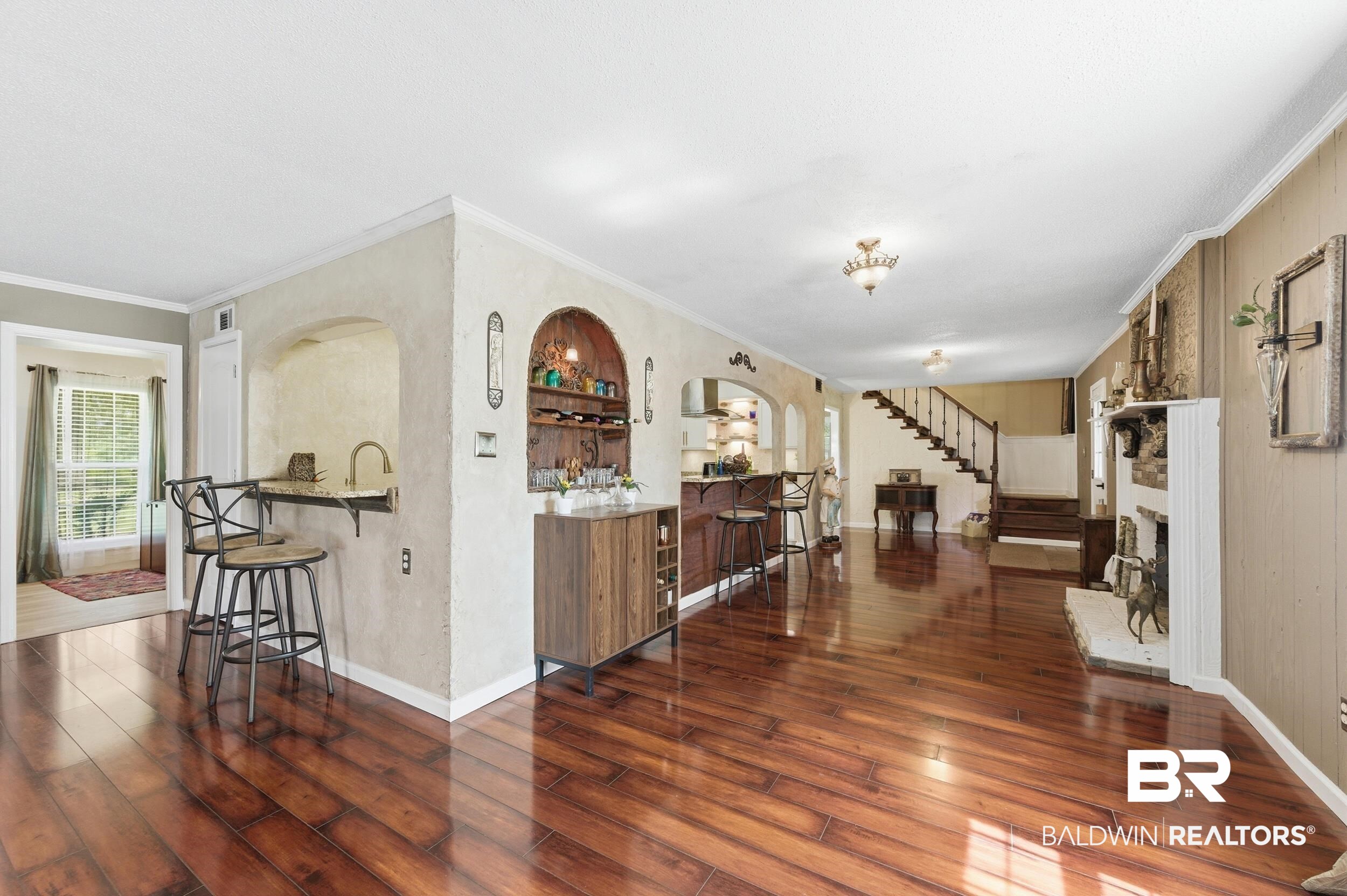 51620 Robert White Road Bay Minette, AL 36507 - Photo 18 of 81 Expansive living area featuring rich wood-finish flooring, a built-in wet bar with stone countertop, a fireplace with a white mantel, and a staircase with wood newel posts and handrail