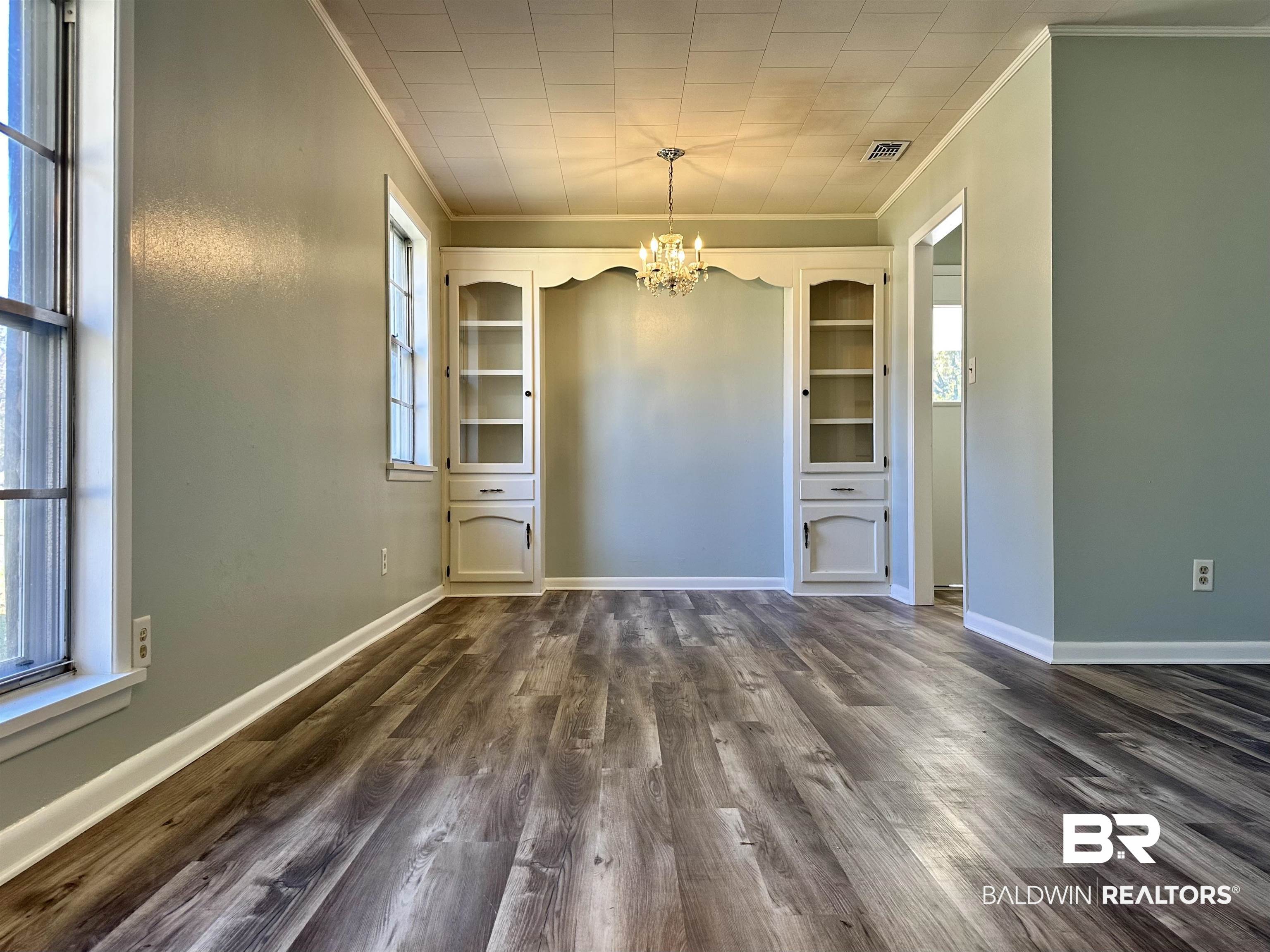 103 Avalon Street Brewton, AL 36426 - Photo 2 of 14 Unfurnished dining area with crown molding, dark wood-type flooring, a healthy amount of sunlight, and an inviting chandelier