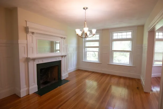 a view of an empty room with wooden floor fireplace and a window