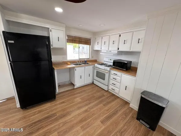 a kitchen with white cabinets a sink a stove a refrigerator and wooden floor