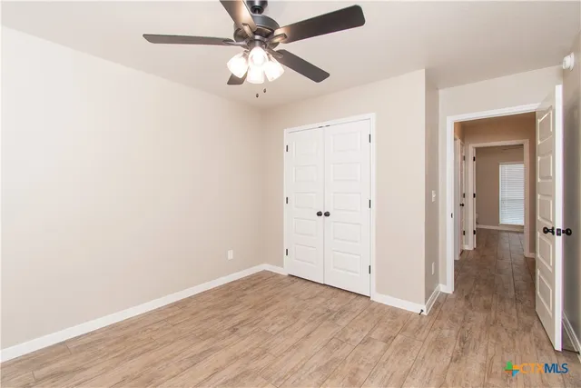 an empty room with wooden floor fan and windows