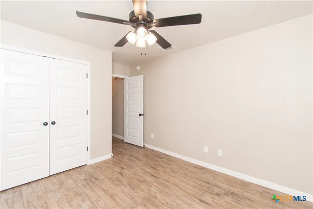an empty room with wooden floor fan and windows