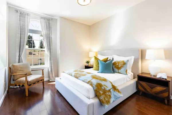 a bed sitting in a bedroom next to a window with chair and wooden floor