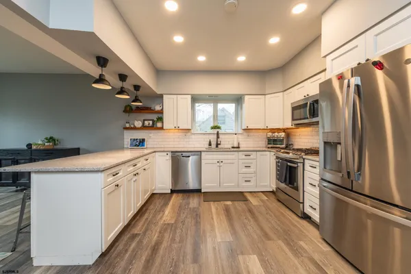a living room with stainless steel appliances furniture a rug kitchen view and a large window