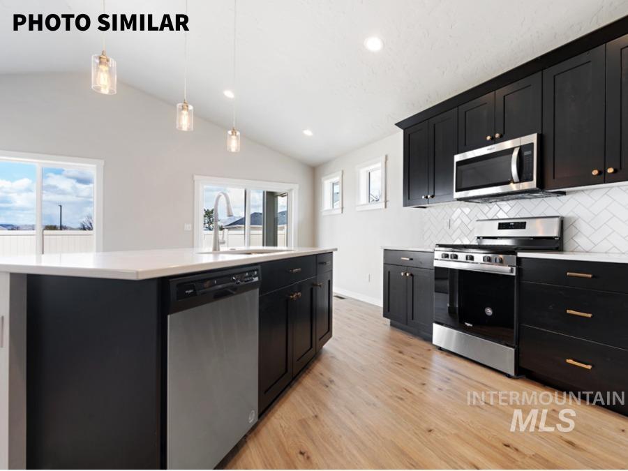 925 Twilight Weiser, ID 83672 - Photo 14 of 31 Modern kitchen featuring dark cabinetry, stainless steel appliances, a white subway tile backsplash, light wood-finish flooring, and a central island with a built-in sink and dishwasher