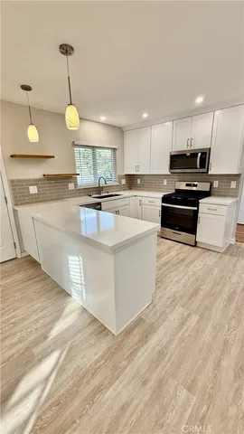 a large kitchen with kitchen island a stove a sink a refrigerator and white cabinets with wooden floor