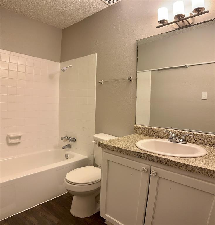 5426 Menchaca Road, Unit 125 Austin, TX 78745 - Photo 6 of 8 Bathroom featuring a white bathtub, white tiled shower surround, dark wood-finish flooring, and a vanity with a light-colored speckled countertop