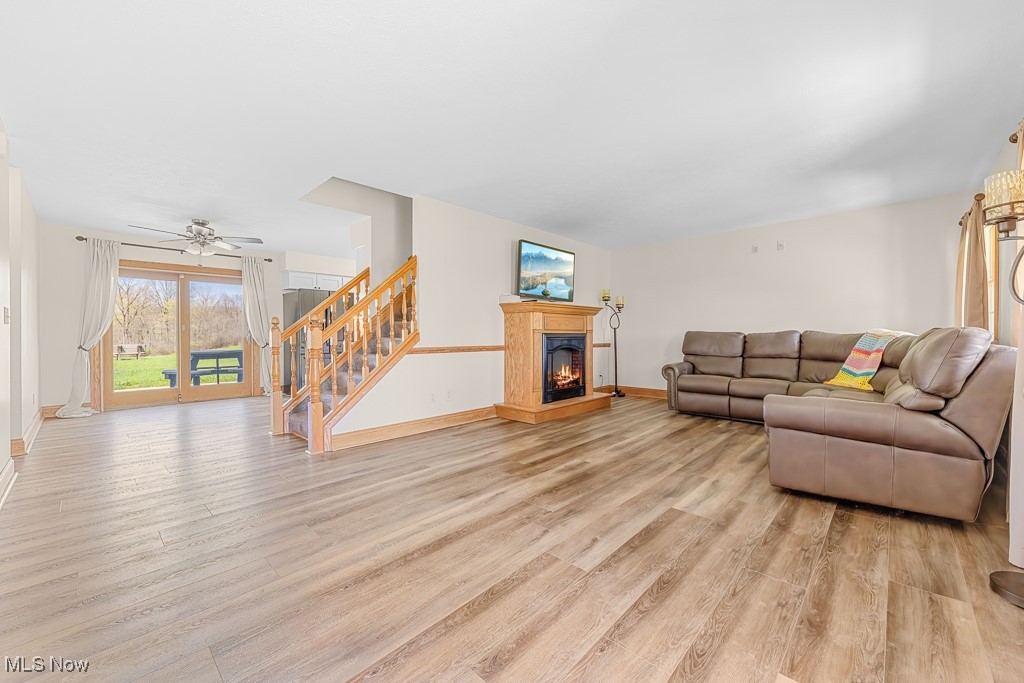 8690 Friendsville Road Lodi, OH 44254 - Photo 11 of 50 Living room featuring baseboards, stairs, light wood-style floors, and a warm lit fireplace