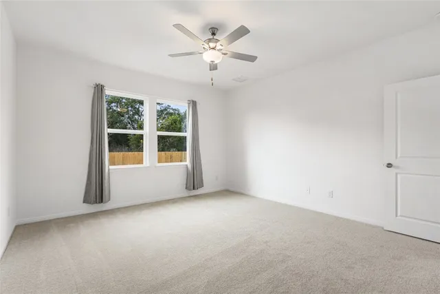 an empty room with chandelier fan and windows
