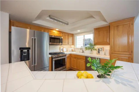 a kitchen with stainless steel appliances kitchen island granite countertop a refrigerator a stove top oven a sink dishwasher and white cabinets with wooden floor