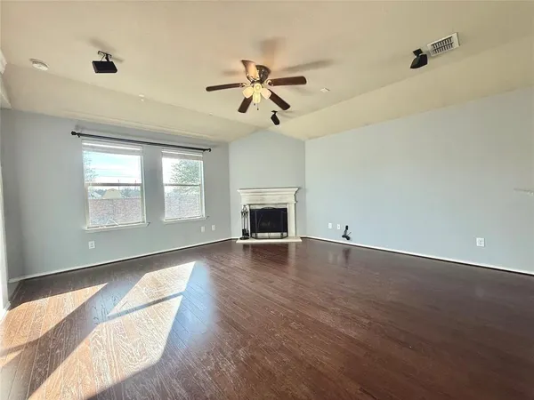 an empty room with wooden floor ceiling fan and windows