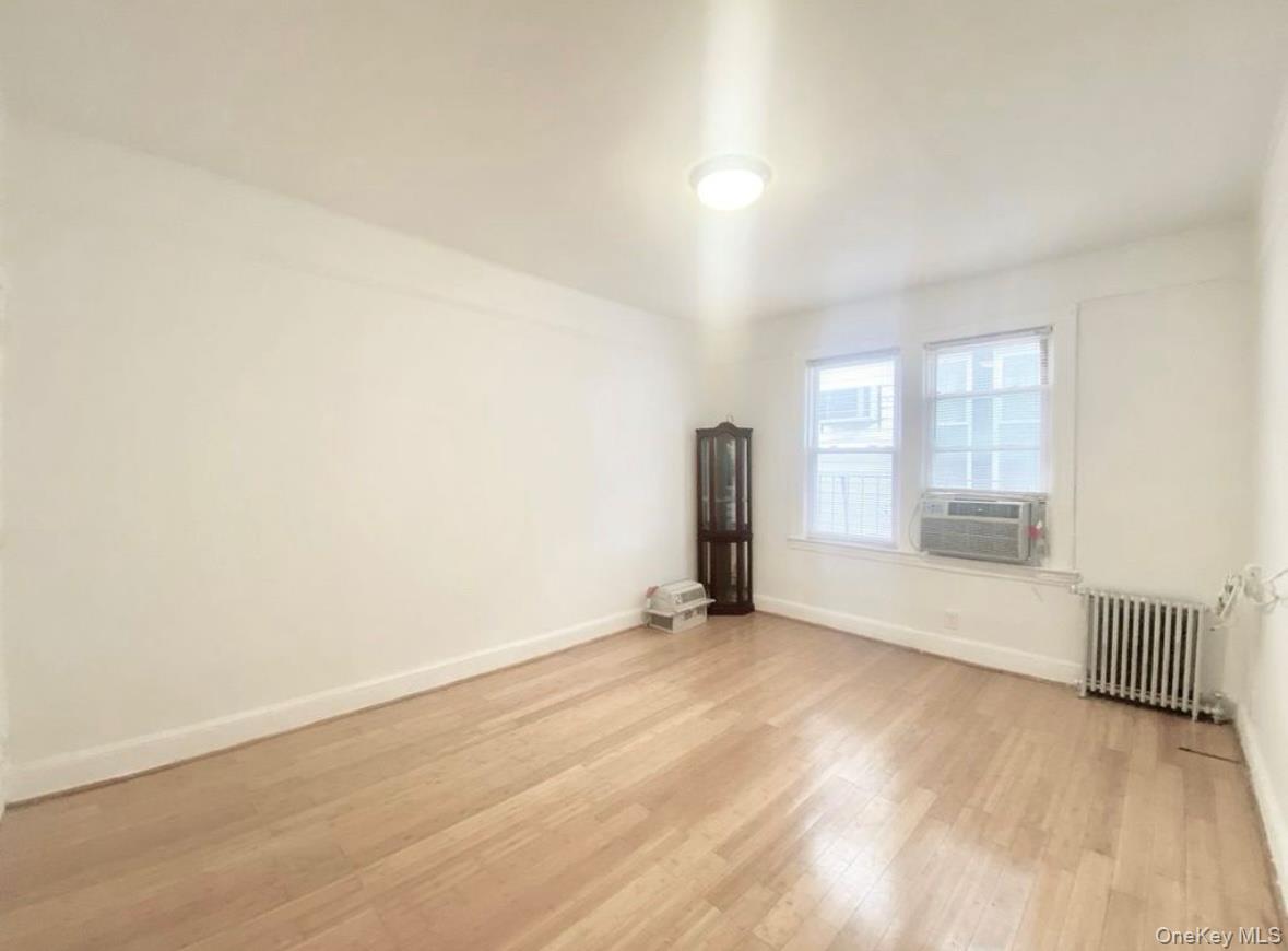 50-24 39th Place Queens, NY 11104 - Photo 5 of 10 Spare room featuring radiator, light wood-style flooring, and cooling unit