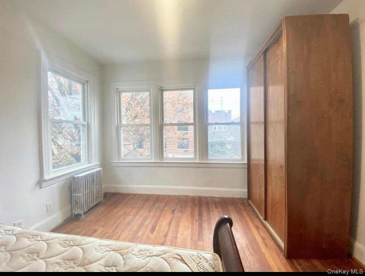 50-24 39th Place Queens, NY 11104 - Photo 8 of 10 Bedroom with radiator heating unit, light wood-style floors, multiple windows, and a closet