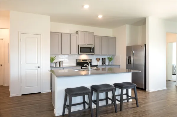 a kitchen with stainless steel appliances granite countertop a dining table chairs refrigerator and microwave