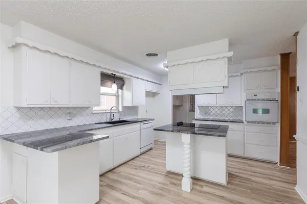 a kitchen with a sink dishwasher a stove and white cabinets with wooden floor
