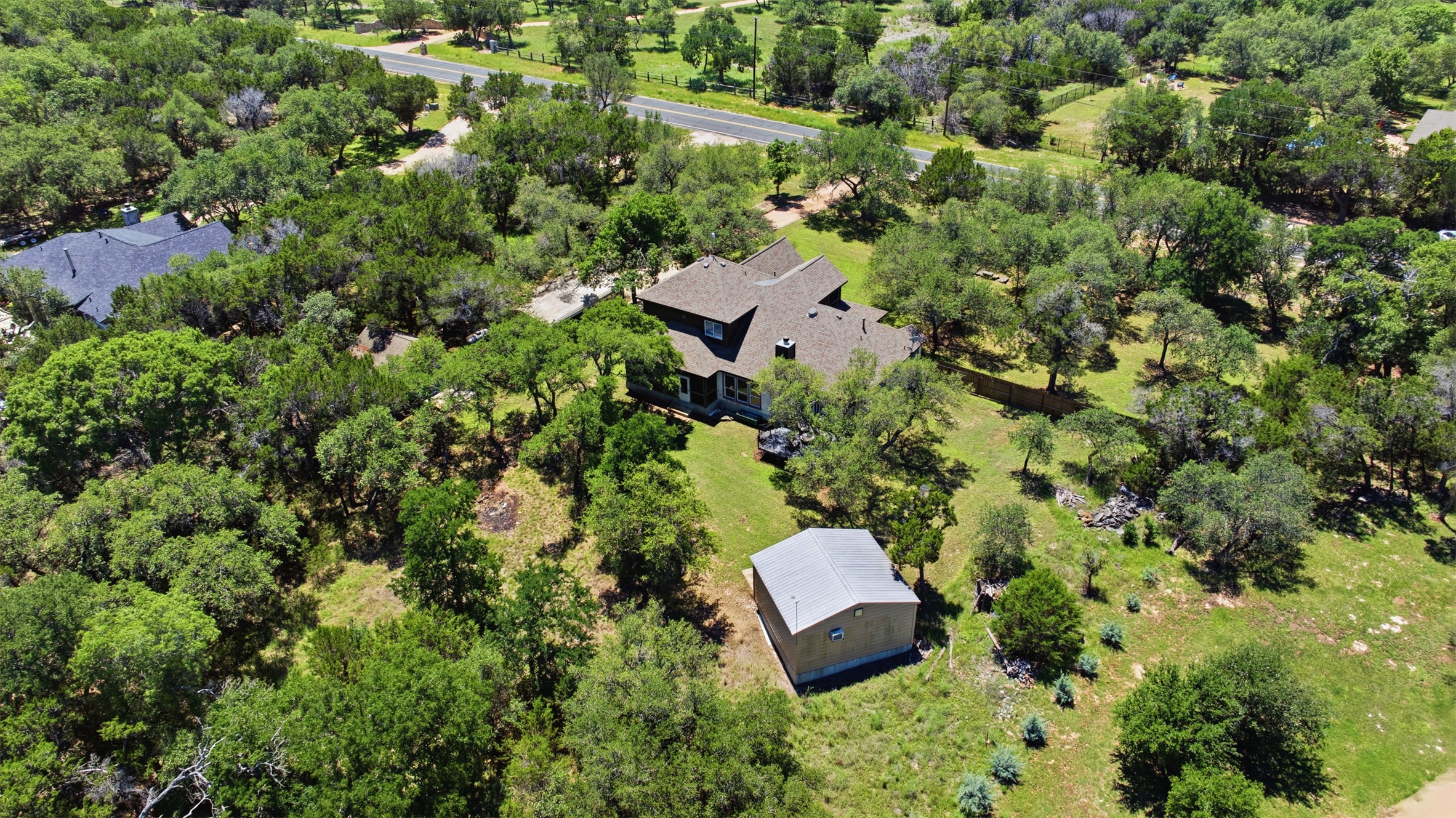 1301 County Road 262 Georgetown, TX 78633 - Photo 4 of 39 Expansive property featuring a multi-level home with a brown shingle roof, a detached utility building with a metal roof, extensive tree coverage, and a clear grassy area