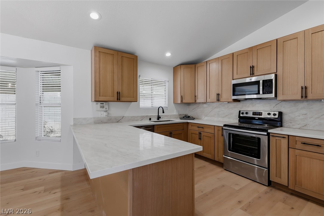 434 Crestway Road Henderson, NV 89015 - Photo 15 of 46 Kitchen featuring stainless steel appliances, light wood-type flooring, a peninsula, lofted ceiling, and decorative backsplash
