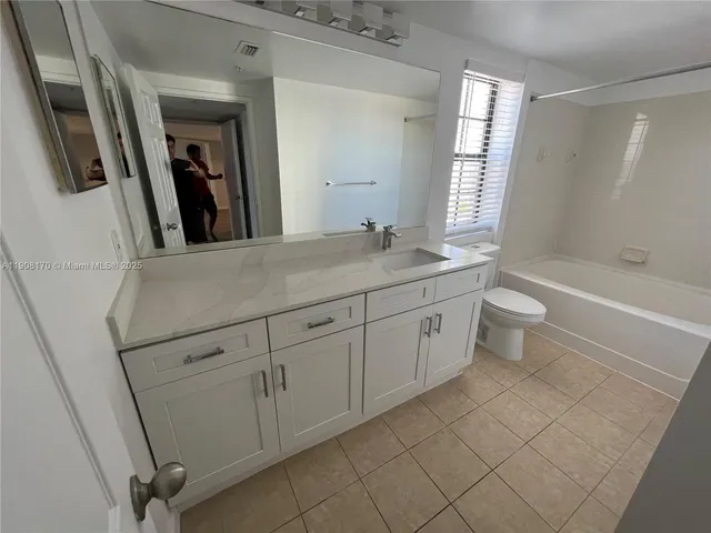 a bathroom with a granite countertop sink a toilet a mirror a bathtub and window