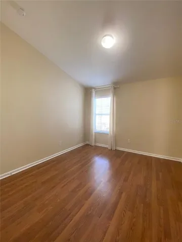 a view of an empty room with wooden floor and window