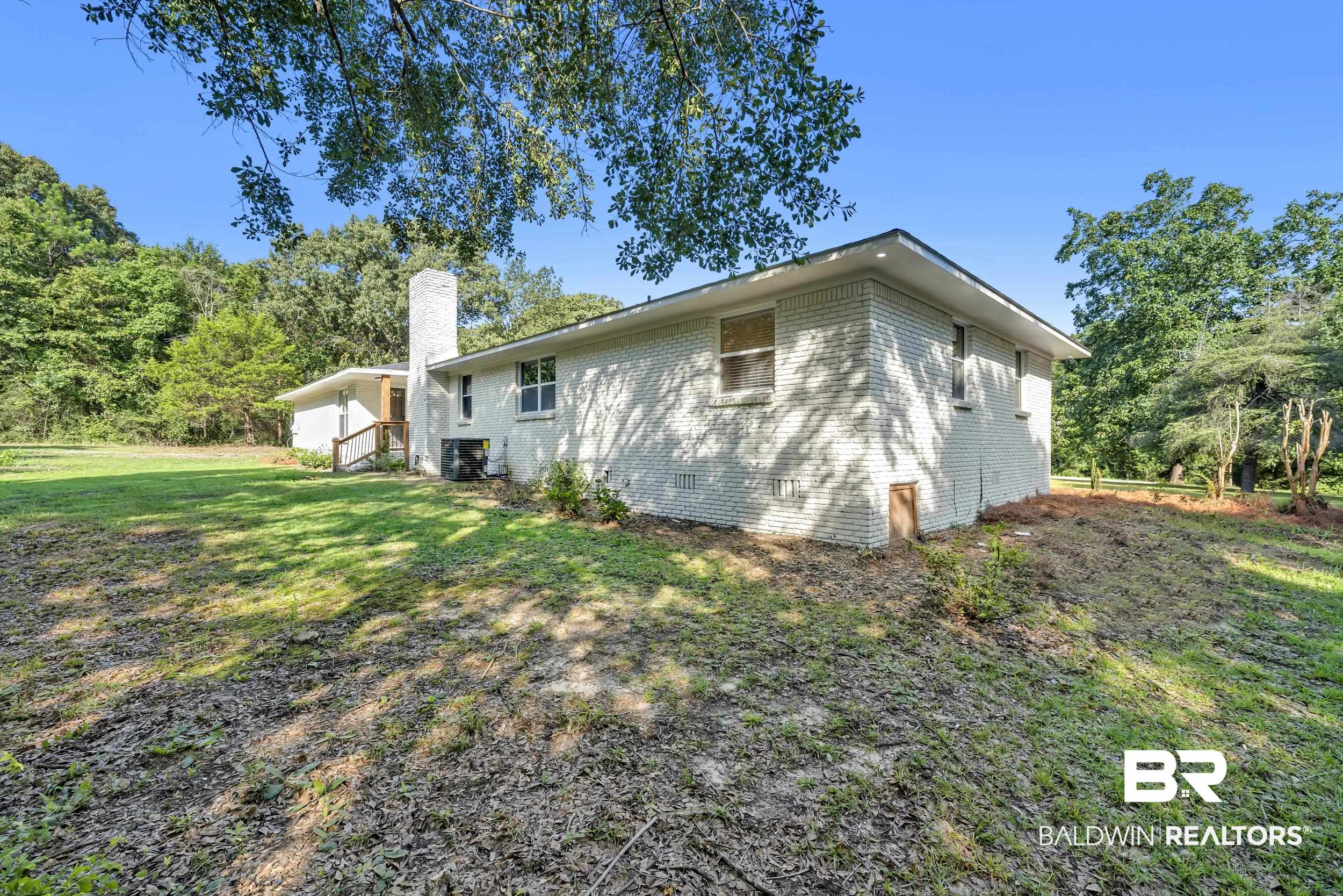 8170 Wilmer Georgetown Road Wilmer, AL 36587 - Photo 25 of 31 White brick exterior with a prominent brick chimney, multiple windows, and a sloped roofline