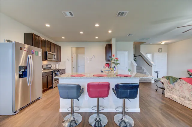 a kitchen with stainless steel appliances kitchen island granite countertop a refrigerator a stove a chairs with wooden floor and cabinets