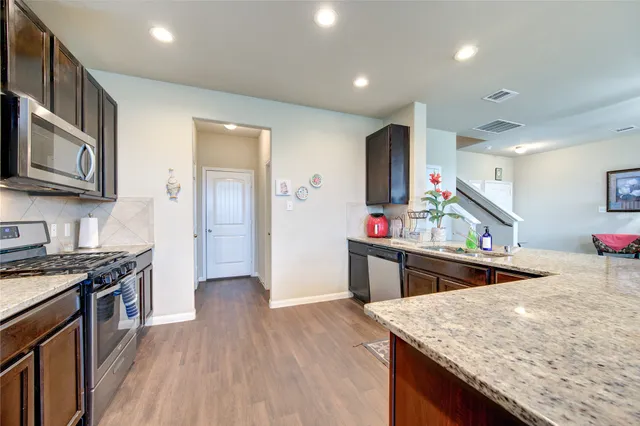 a kitchen with stainless steel appliances granite countertop hardwood floor sink stove and wooden cabinets