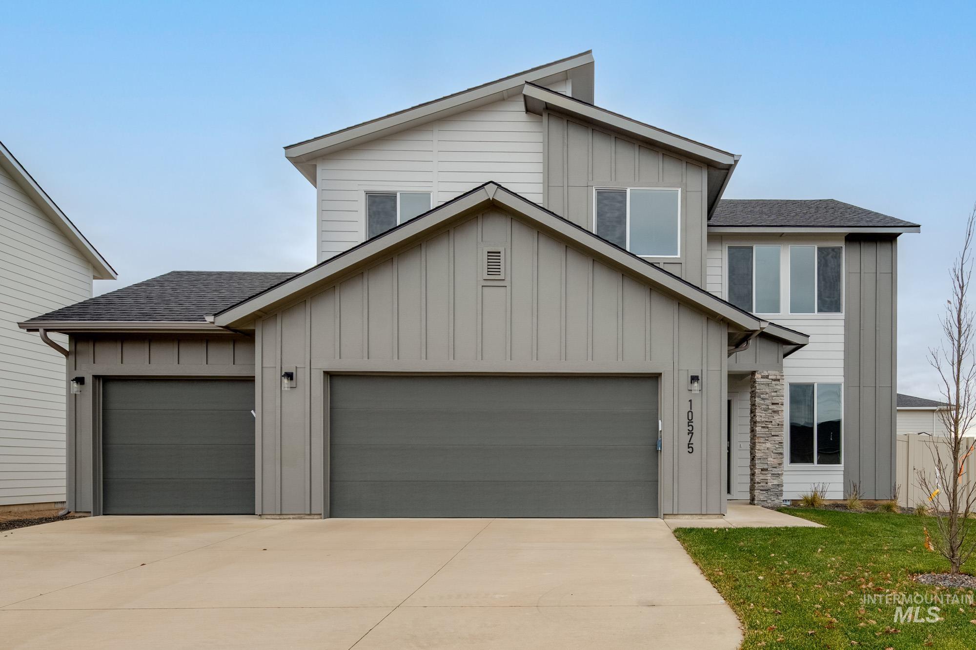 View of front of property with board and batten siding, roof with shingles, an attached garage, driveway, and a front lawn