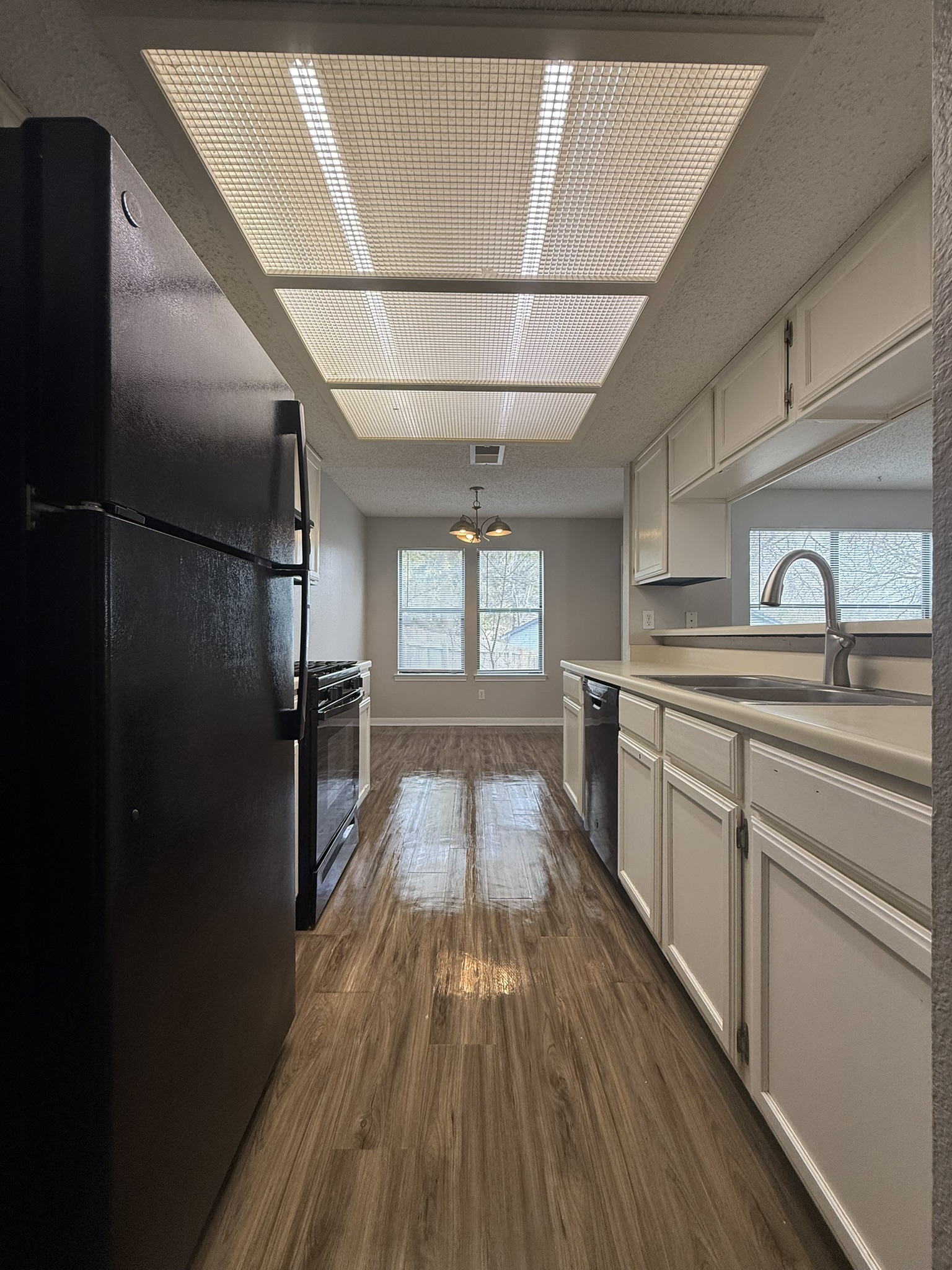 7806 Topawa Cove, Unit A Austin, TX 78729 - Photo 14 of 25 Kitchen with black appliances, white cabinetry, dark wood finished floors, and light countertops